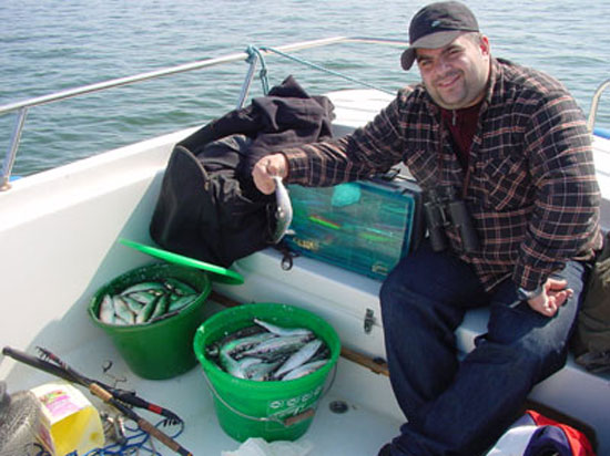 Tuncay, stolz mit dem Tagesfang, in der Hand einen weiteren Hering an der Schwanzflosse haltend